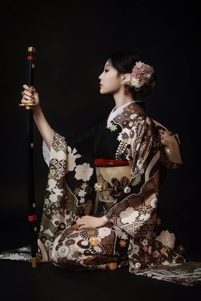 黑地金色花纹和服,手持刀鞘侧身而坐,深色背景的人像