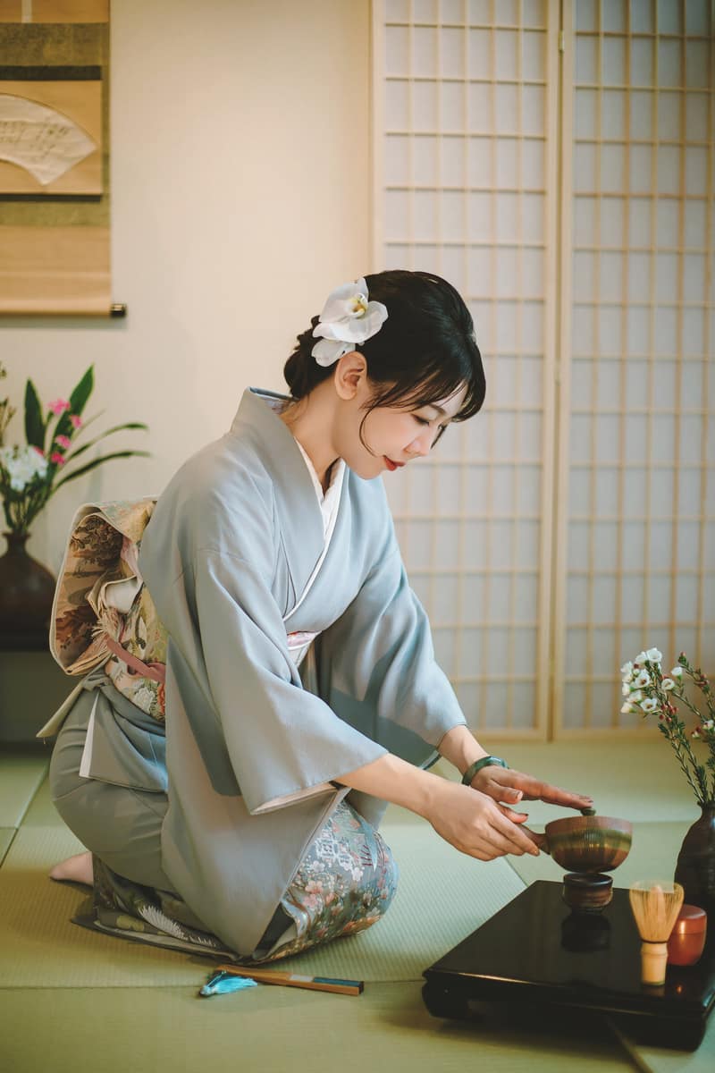 水色和服在和室点抹茶,身旁是茶筅与茶枣,背景为障子与挂轴