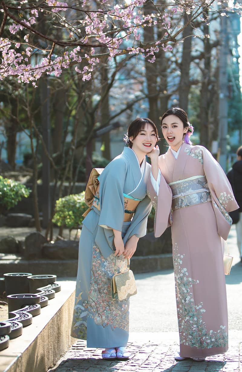 桜の下の石畳で並んで立つお二人。水色に鶴の着物と、白い小花を散らした薄紅の着物