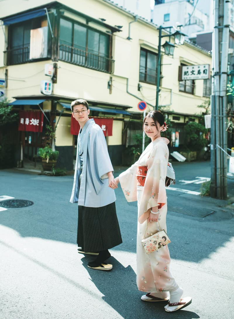 浅草の街角で振り返るお二人。男性は淡い水色の羽織に縞の袴、女性は淡い桜色の着物
