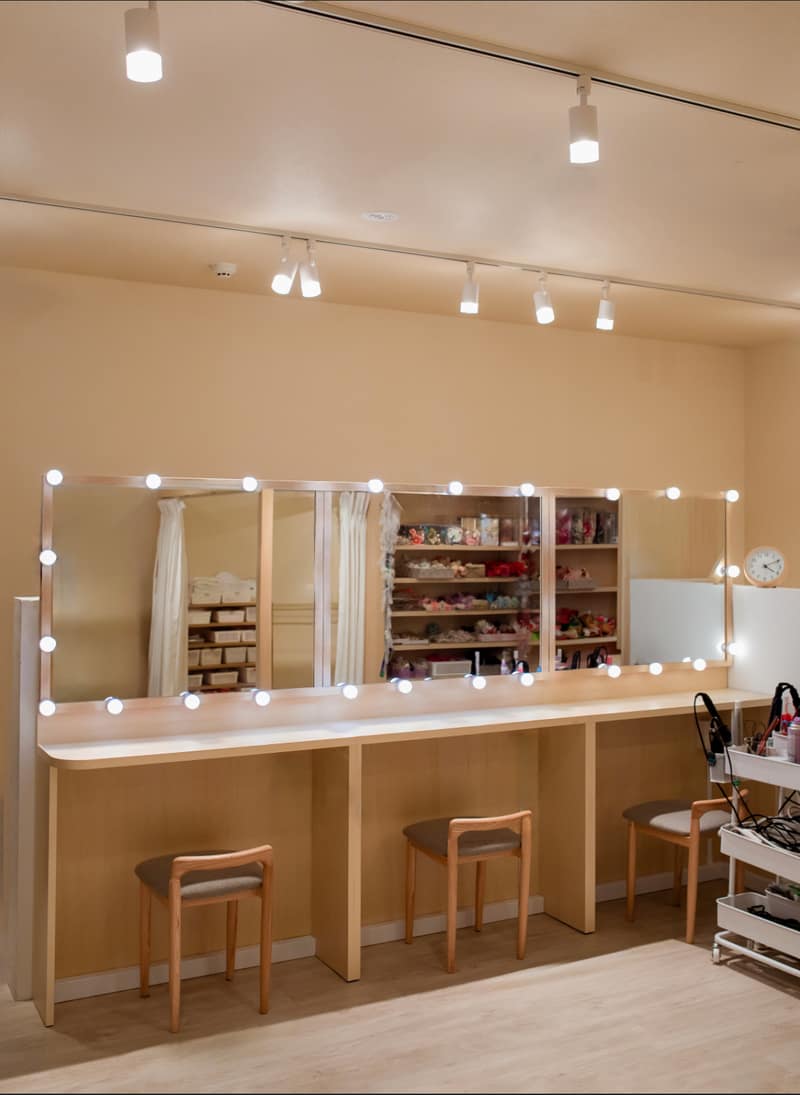 A hair and make-up counter lined with bulb-framed mirrors and wooden stools