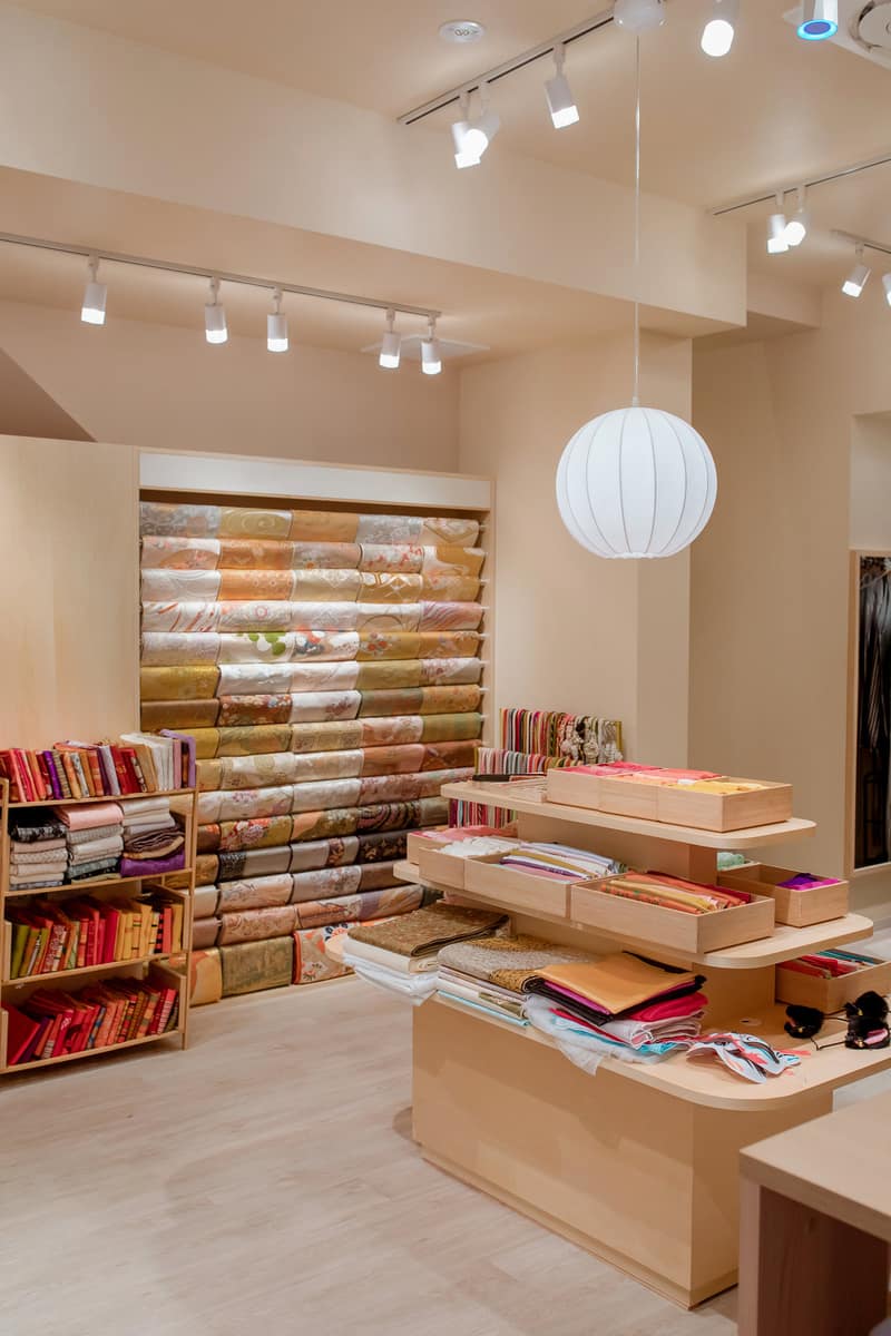 Shop interior with a wall of stacked obi, wooden display tables and a round paper lamp