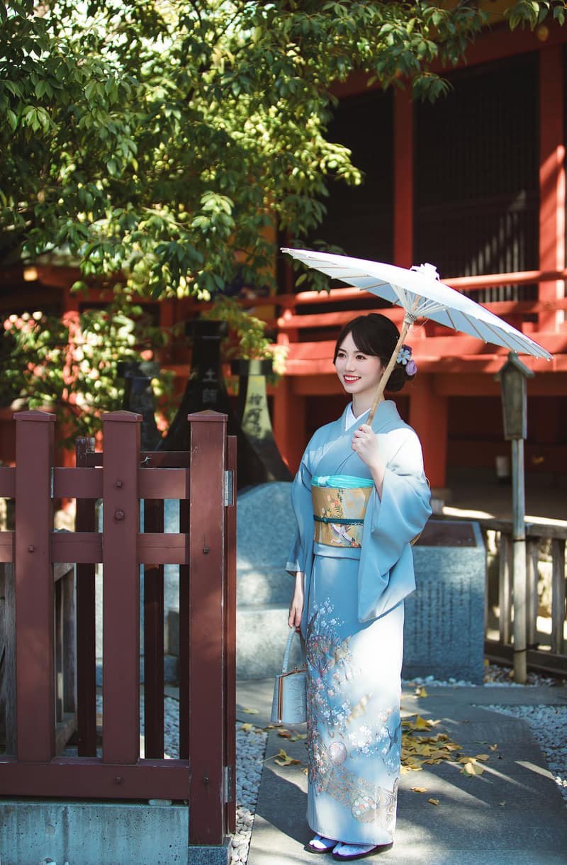Pale blue irotomesode patterned only below the waist, with a white paper parasol by a vermilion shrine hall