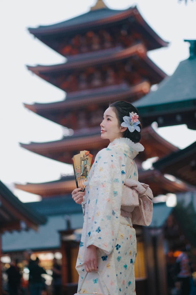 Ivory lace kimono scattered with pastel butterflies and flowers, worn with a folding fan, five-storey pagoda behind